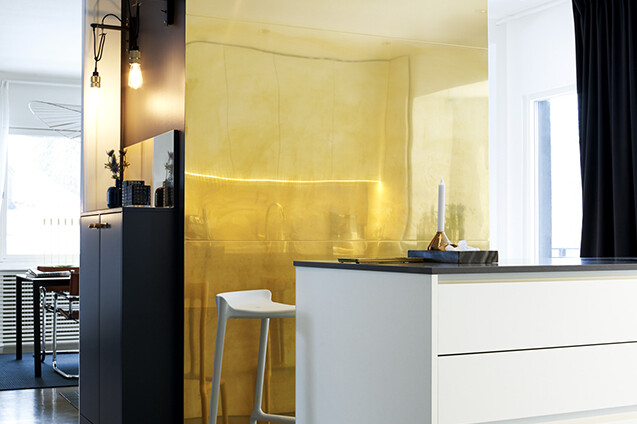 Köksö med vita köksluckor och en guldfärgad vägg bakom