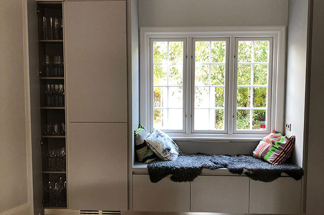 Utrymme i ett hem med inbyggd soffa med färgglada kuddar, vid fönster och förvaring med vinglas bredvid