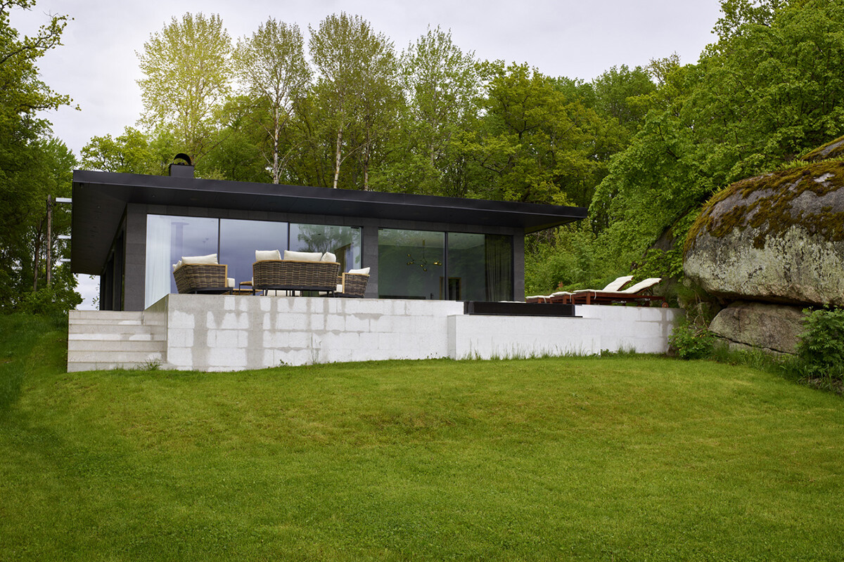 Modern, svart villa med stor altan och grön trädgård
